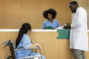 il team di medici e infermieri afroamericani incoraggiano allegramente il paziente con osteoartrite in sedia a rotelle al suo appuntamento in ospedale per la terapia fisica dopo un intervento chirurgico al ginocchio foto