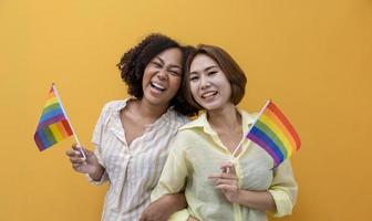 coppia di matrimonio dello stesso sesso che tiene la bandiera arcobaleno lgbtq per il mese dell'orgoglio per promuovere l'uguaglianza e le differenze del concetto di omosessualità e discriminazione isolati su sfondo giallo foto