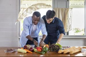 diversità di genere di lgbtq coppia gay tra etnia asiatica e africana che cucinano insieme a casa usando verdure biologiche per preparare insalata e sandwich foto