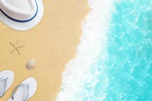 composizione spiaggia vista dall'alto con cappello, pantofole, stella e conchiglia sulla sabbia con onda del mare accanto foto