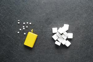 confrontando il dolcificante artificiale con lo zucchero bianco su sfondo nero foto