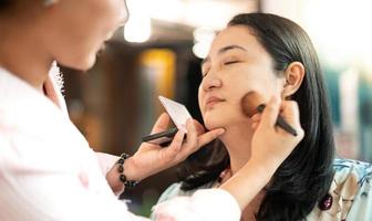 la giovane bella asiatica prepara l'applicazione del trucco dal truccatore professionista. foto