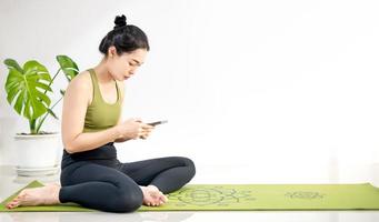 donne che giocano al cellulare e si siedono sul tappetino da yoga verde mentre riposano per una pratica in casa. foto