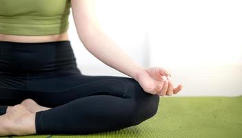 donna che pratica lezione di yoga, respira, medita seduta su un tappetino da yoga verde, in casa. foto