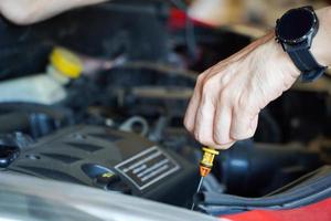 meccanico asiatico che ripara auto con cofano aperto, vista laterale del meccanico che controlla il livello dell'olio motore in un'auto con cofano aperto foto