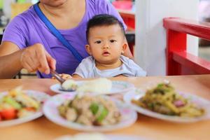 madre che dà da mangiare a suo figlio durante il pranzo al ristorante. bambino asiatico che mangia con la madre. foto