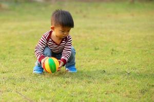 ragazzo asiatico che gioca a calcio al parco. bambino con palla giocattolo nel campo in erba. foto