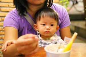 madre che dà da mangiare a suo figlio durante la cena al ristorante. bambino asiatico che mangia con la madre. foto