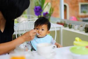 madre che nutre cibo a suo figlio durante la colazione al ristorante. bambino asiatico che mangia con la madre. foto