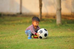 ragazzo asiatico che gioca a calcio al parco. bambino con palla giocattolo nel campo in erba. foto