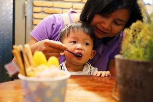 madre che dà da mangiare a suo figlio durante la cena al ristorante. bambino asiatico che mangia con la madre. foto