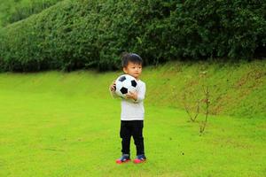 ragazzo asiatico che tiene palla in mano al parco. bambino che gioca a calcio. foto