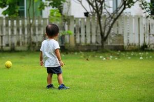 ragazzo asiatico che gioca a calcio al parco. bambino con la palla nel campo in erba. foto