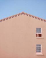 vista frontale della casa a timpano con parete rosa e cielo blu.concetto minimo.rendering 3d foto