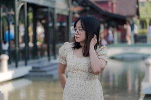 la donna asiatica con gli occhiali si tocca i capelli e pensa vicino al fiume in una città colorata, foto