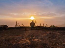 alba nella nebbia cielo nuvoloso sulla collina con raggio di sole a phatang 104 punto di vista picco di montagna con turista donna seduta e guardando la vista. viaggiare a chiang rai, tailandia foto