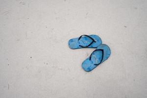 un paio di sandali a pantofola di gomma blu sulla spiaggia di sabbia bianca, foto