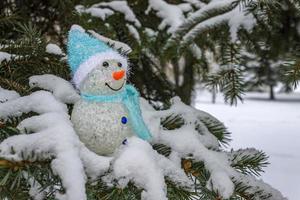 un pupazzo di neve giocattolo si erge sui rami spinosi innevati di un abete nella foresta in inverno foto