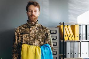 soldato patriota ucraino in uniforme militare che tiene una bandiera gialla e blu in ufficio foto