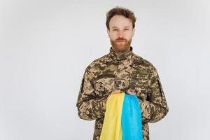 Soldato patriota ucraino in uniforme militare che tiene una bandiera gialla e blu su sfondo bianco foto