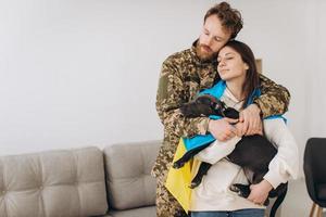 una coppia ucraina, un soldato in uniforme militare e una ragazza avvolta in una bandiera ucraina tengono in braccio un cane, felici insieme. foto