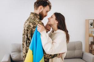 una ragazza ucraina abbraccia e tiene in mano una bandiera gialla e blu di un militare in uniforme e lo saluta. foto