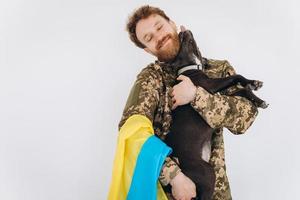 il soldato ucraino in uniforme militare con una bandiera gialla e blu tiene un cane in braccio su uno sfondo bianco foto