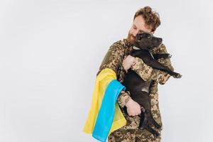 il soldato ucraino in uniforme militare con una bandiera gialla e blu tiene un cane in braccio su uno sfondo bianco foto