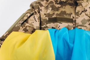 ritratto di un giovane soldato patriota ucraino barbuto emotivo in uniforme militare che tiene una bandiera in ufficio foto