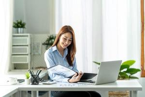 giovane bella donna che usa il suo laptop mentre era seduto su una sedia al suo posto di lavoro. foto