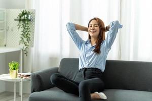felice donna asiatica rilassante seduta sul divano a casa, lavoro da casa concetto. foto