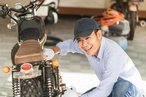 meccanico allegro che ripara moto nel garage dell'officina, uomo sorridente che ripara la moto in officina, concetti di riparazione e manutenzione foto