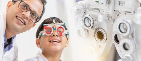 stile banner, ragazzo indiano-tailandese sorridente che sceglie gli occhiali nel negozio di ottica, ragazzo che fa un esame della vista che controlla l'esame con l'ottico optometrista che usa la montatura di prova nel negozio di ottica foto