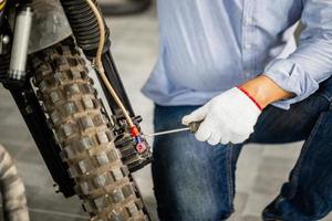 mani del tecnico maschile utilizzando un cacciavite che fissa e ripara la motocicletta in officina, meccanico che ripara la moto nel garage dell'officina, concetti di riparazione e manutenzione foto