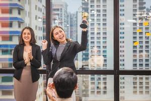 la donna d'affari che tiene il trofeo del premio mostra la vittoria nella sala riunioni, concetti di squadra di felicità di successo di celebrazione foto