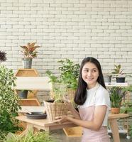 ritratto bella ragazza asiatica piuttosto giovane donna che indossa una camicetta bianca con lunghi capelli neri e bella, sorridente con un sorriso luminoso e guardando piccolo albero nella stanza della piantagione di alberi felicemente e rilassato foto