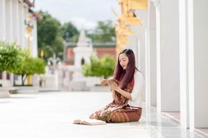 donna buddista asiatica che indossa abiti tradizionali della tailandia che legge il sanscrito antico libro tripitaka del signore buddha dhamma e libro del dharma, santuario ratchanatdaram bangkok. foto