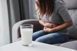 donna che ha mal di stomaco con un bicchiere di latte, intolleranza al lattosio, concetto di assistenza sanitaria foto