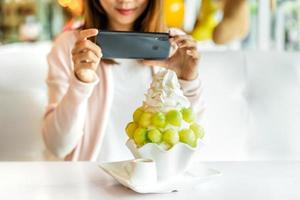 giovane donna che scatta foto di bingsu con uno smartphone nel ristorante e carica le foto sui social media