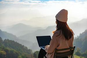 viaggiatore freelance di giovane donna che lavora online utilizzando il laptop e godersi il bellissimo paesaggio naturale con vista sulle montagne all'alba foto