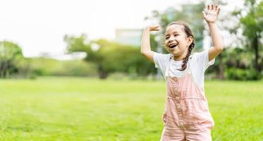 ragazza felice del bambino che sorride e alza la mano mentre si trova nel parco, bambina che si gode una calda giornata nel parco autunnale foto