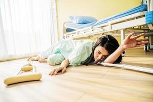 il paziente asiatico femminile è caduto sdraiato sul pavimento in ospedale. sta cercando di alzare la mano e chiedere aiuto, c'è stata un'asta di supporto caduta sul pavimento di legno, incidente o altra salute foto