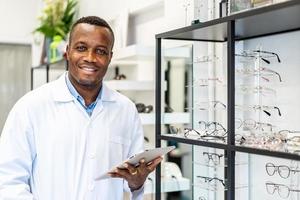 concetto di vista e visione. vista dell'ottico attraente afroamericano sorridente che lavora con il tablet nel suo negozio di occhiali. foto