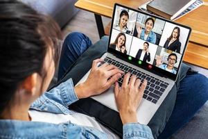 team aziendale che lavora da casa in una videoconferenza. la vista posteriore di una ragazza che comunica online in videoconferenza con i suoi colleghi di lavoro utilizzando un laptop a casa foto