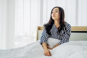 triste donna asiatica sola a casa quarantena di autoisolamento per la prevenzione dell'allontanamento sociale del coronavirus covid-19, lei seduta sul letto si sente noiosa in camera da letto, salute mentale. foto