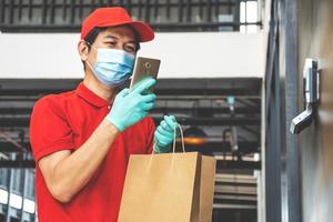 consegna di cibo, monitoraggio degli ordini, covid-19 e concetto di auto-quarantena. corriere che controlla l'indirizzo del cliente sul telefono come portare l'ordine del cibo, chiamando il cliente, sfondo dell'ufficio in piedi foto