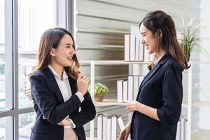 sorridente due donne d'affari che parlano con il partner mentre si trovano in un moderno ufficio interno, team di dipendenti professionisti che discutono idee di progetto dopo l'incontro foto