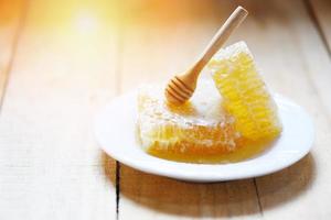 miele fresco, miele delle api cibo sano giallo dolce fetta a nido d'ape con mestolo di legno su piatto bianco sullo sfondo di legno foto