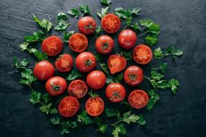 mezzo pomodoro e prezzemolo verde intorno su sfondo scuro. ingredienti freschi per fare l'insalata vegetariana. verdure dell'orto raccolte foto