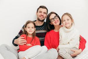 ritratto di famiglia madre, padre e due sorelle guardano direttamente nella fotocamera, hanno espressioni positive, si abbracciano e sorridono con gioia, isolati su sfondo bianco. girato in studio. relazione foto